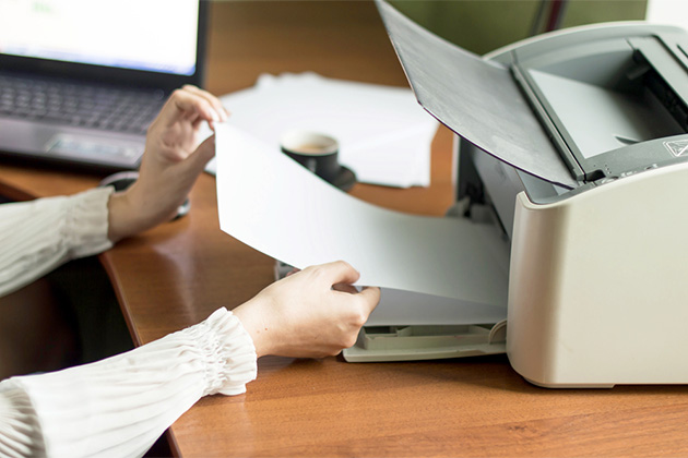 Print out your travel documents (Photo: Gorvik/Shutterstock) Woman taking paper out of printer