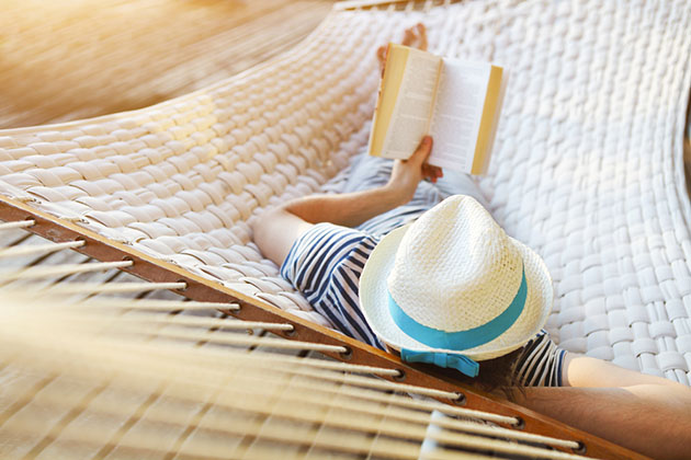 17 Best Cruise Books (Photo: Dasha Petrenko/ Shutterstock) 17 Man in hat in a hammock on a cruise deck with book on a summer day