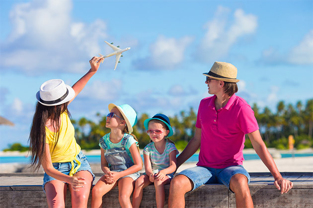 Reasons to fly in early (Photo: TravnikovStudio/Shutterstock) Family in tropical destination flying a toy plane