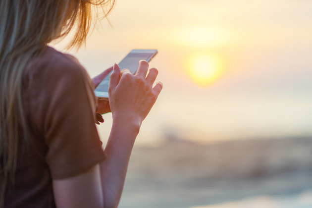 19 Cruise Apps You Need Right Now (Photo: tolotola/Shutterstock.com) woman texting on smart phone on the beach during sunset