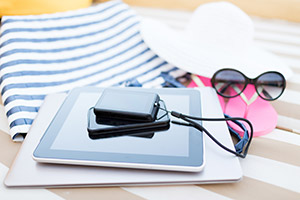 Technologist's vacation packing list - photo courtesy of Syda Productions/Shutterstock vacation and technology - close up of tablet pc computer, smartphone, camera and summer accessories on a beach chair